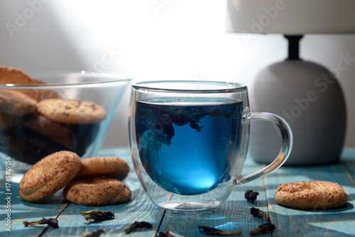Blue butterfly pea tea in glass cup with cookies on blue wooden table