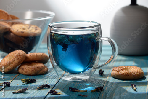 Blue butterfly pea tea in glass cup with cookies on blue wooden table