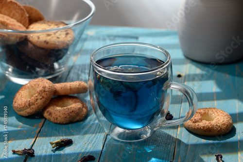 Blue butterfly pea tea in glass cup with cookies on blue wooden table