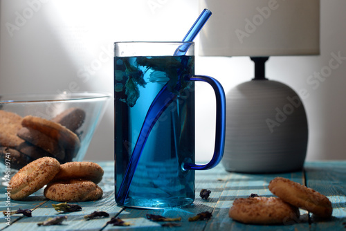 Blue butterfly pea tea in glass cup with cookies on blue wooden table
