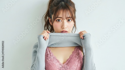 白い壁の前でセーターからピンクのレースの下着を見せる若い女性