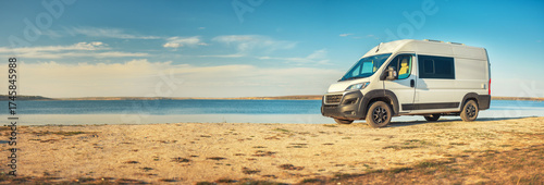 Panoramic view to sea coast with white camper van on wild beach with copy space