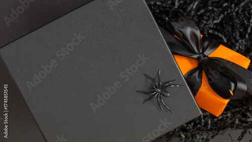 Stylish Halloween composition with black gift box, plastic spider, and orange present tied with black ribbon on dark background. Elegant spooky flat lay design for festive decor and holiday mood.