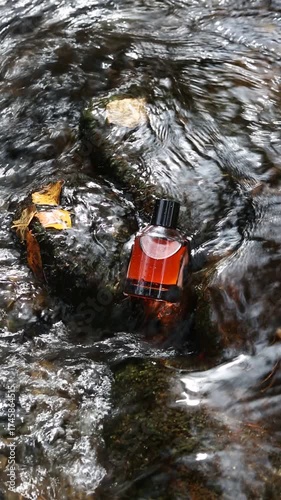 Perfume bottle with warm amber tones set on a glistening stone in gentle flowing water. Modern advertising composition