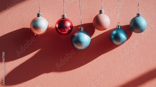 Colorful Christmas ornaments hang on peach wall casting long shadows for festive decor