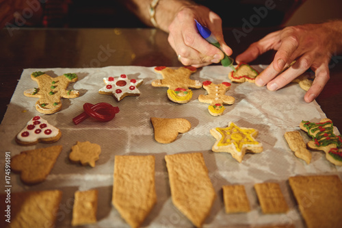 Family Christmas Cookies Decorating Scene: Hands Pipe Icing on Star, Tree, Heart Shapes in Warm Kitchen During Holiday Baking