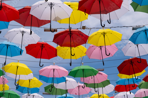 Colorful umbrellas hanging in the sky. Vibrant street decoration with umbrellas. Creative urban decor with hanging umbrellas.