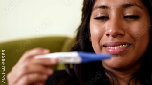 Woman holding pregnancy test, looking hopeful, in a room, can be used for healthcare