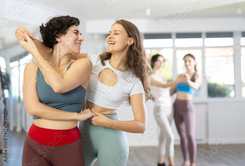 Two enthusiastic young women enjoying in brightly-lit dance studio, energetically moving to rhythm of salsa as dance partners..