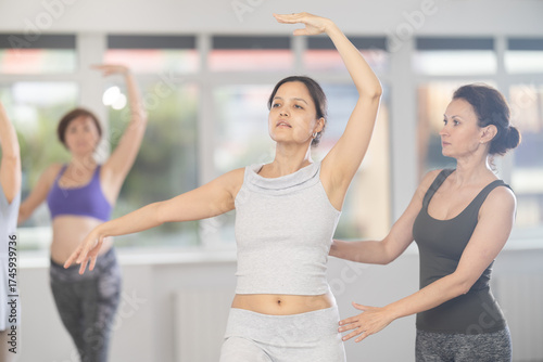 Expressive young Asian woman enjoying ballet practice under attentive guidance of experienced female instructor during beginners group class in mirrored choreography studio..