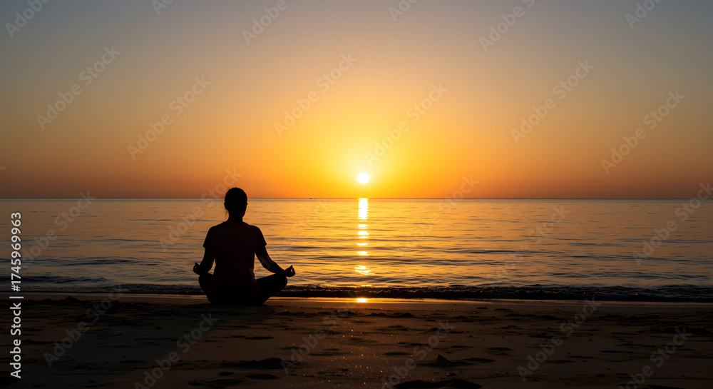 Fototapeta premium Silhouette of a Person Meditating by the Beach During Vibrant Sunset Over Calm Ocean