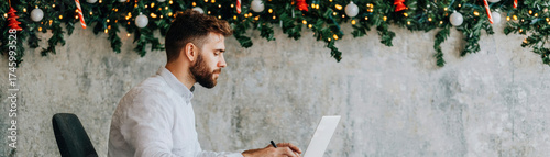 Christmas business double exposure concept with focused man working at laptop under festive holiday decorations and warm lights