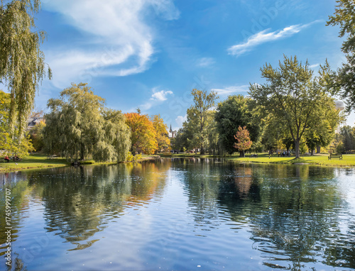 Looking across a lake at an urban park in autumn with willow and hardwood trees in fall colours, church steeple in background