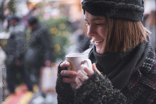 Headshot of beautiful young woman, while going to drink mulled wine out of cup on traditional Christmas market in Cologne, Germany. Portrait of model in winter outfit is enjoying cup of tea or coffee 