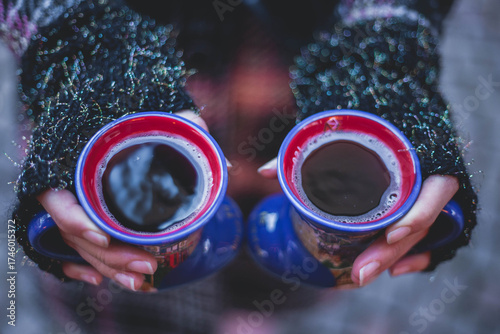 Close up on woman's hans holding two cup of mulled red wine. Females hands holding hot drinks, while wearing fingerless gloves and winter coat. Christmas market concept.