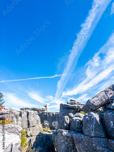 Man sitting on rocky outcrop overlooking wide mountain landscape and dramatic sky with white contrails at Bear Rocks Preserve, Dolly Sods, West Virginia