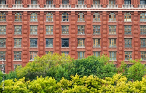 Historic Red Brick Building Facade with Green Trees in Foreground