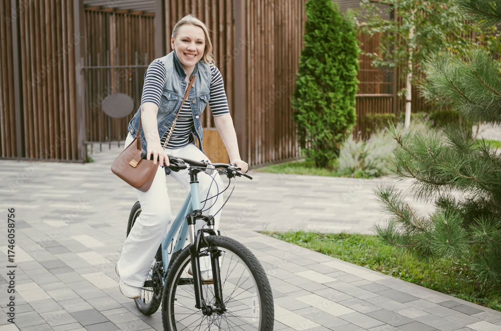 Obraz premium blonde woman rides her bicycle through a modern park, smiling and having fun in her casual clothing on a sunny autumn day