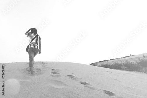 Asian woman lonely walking on small desert mountain and many footprints on the small sand mountain with copy space in black and white style. Loneliness, Alone, Travel nature in monochrome concept.