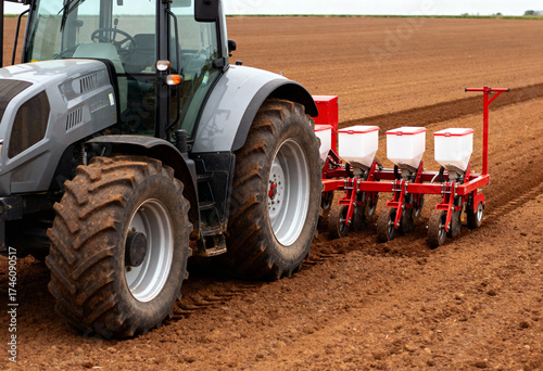 a modern tractor equipped with a seed planting machine operating in a freshly plowed field. 