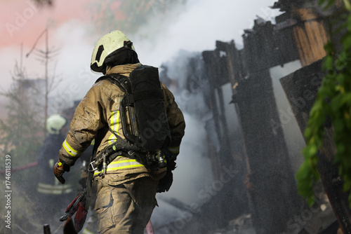 A professional firefighter in helmet and protective suit standing in dense smoke at the scene of fire