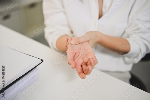 Businesswoman suffering from hand fatigue, rubbing wrist to relieve pain caused by overuse or office work