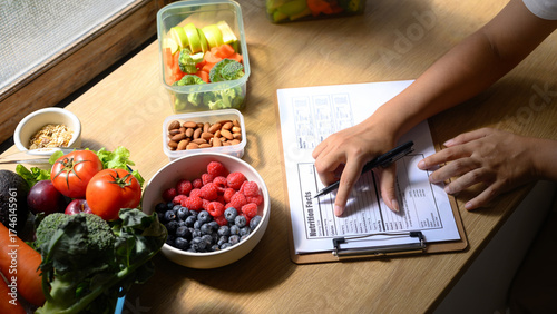 Nutritionist analyzing and writing a healthy meal plan with fresh fruits, vegetables, and nuts on the table