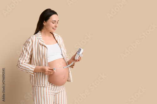 Young pregnant woman with fetal doppler listening to baby's heartbeat on beig...