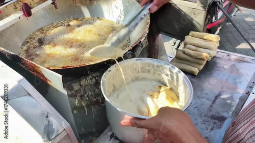 The process of frying bananas by placing batter-dipped bananas into a wok with boiling oil. A popular street food in Indonesia.