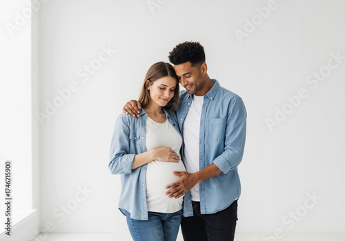Pregnant woman with mixed race partner in matching blue shirts touching belly. Interracial couple maternity session for diverse family planning services