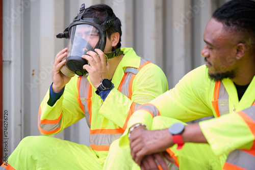 Foto Workers in safety attire, one wearing a gas mask, taking a break in factory