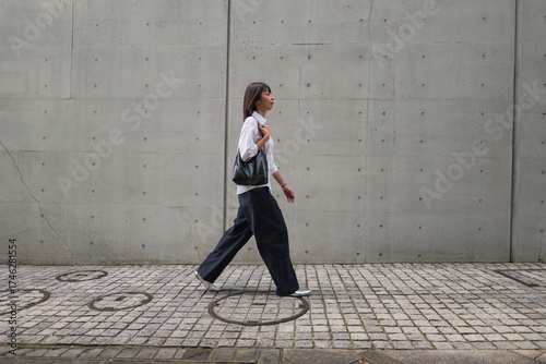Businesswoman walking along a sidewalk with a concrete wall backdrop