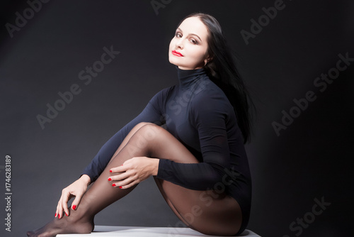 Natural Female's Portraits. Studio Portrait of Tranquil Sexy Caucasian Brunette Woman in Black Body Suit Posing on White Box Against Black
