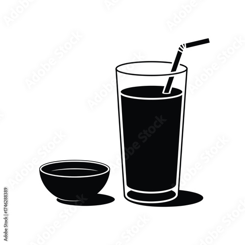 Tall glass of dark beverage with straw and small bowl