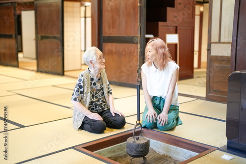 Two women sitting on the floor in a room. One of them is wearing a white shirt. The other woman is sitting on the floor with her legs crossed
