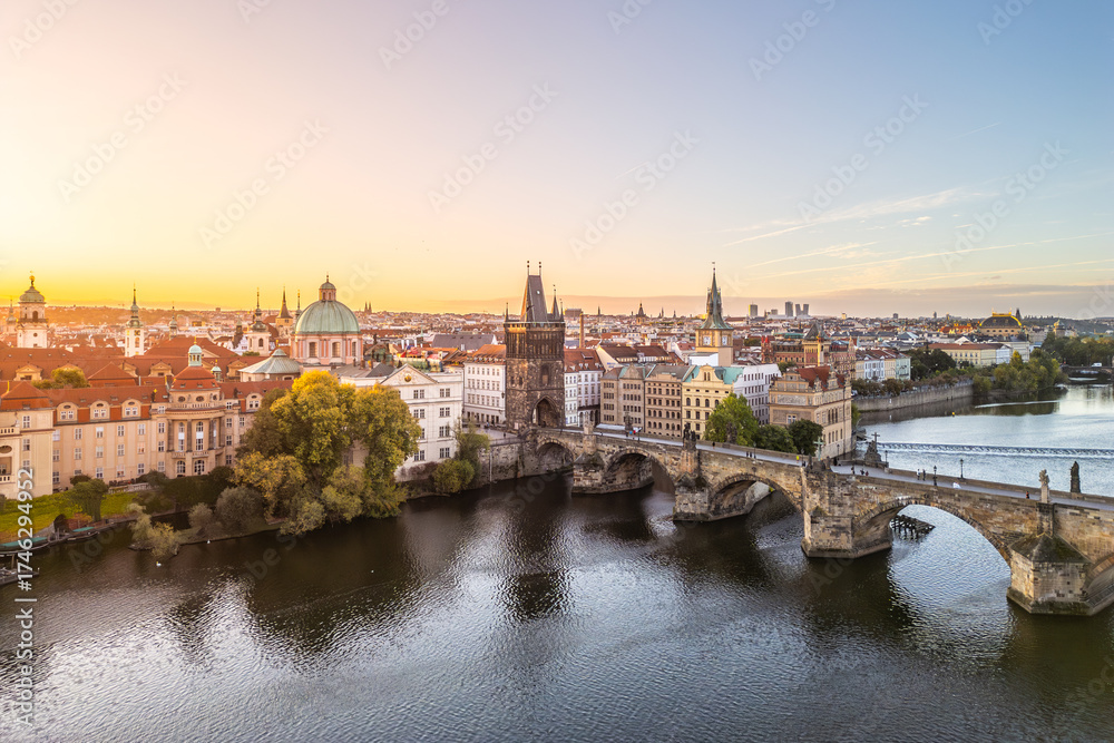 Fototapeta premium Stunning view of Old Town Bridge Tower at Charles Bridge during sunset. The serene Vltava River reflects the historic architecture of Prague, creating a picturesque scene.
