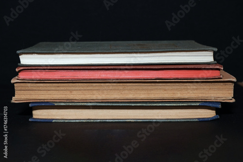 Stack of vintage books with decorative spines and colored edges placed on a black background. Warm tones and soft shadows highlight craftsmanship, history and cultural heritage.
