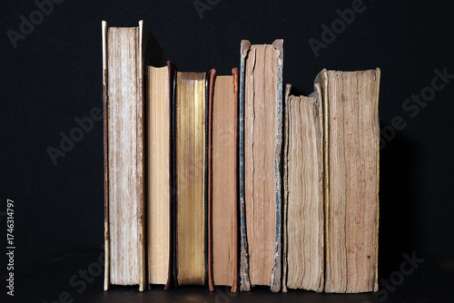 A row of antique books with richly worn covers and golden lettering standing upright on a black background, symbolizing knowledge, history and timeless fascination with literature and culture.