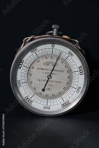 Close-up of a vintage Italian altimeter with metallic dial, engraved numbers and fine needle, illuminated against a dark background. Perfect for illustrating aviation, engineering or retro measurement