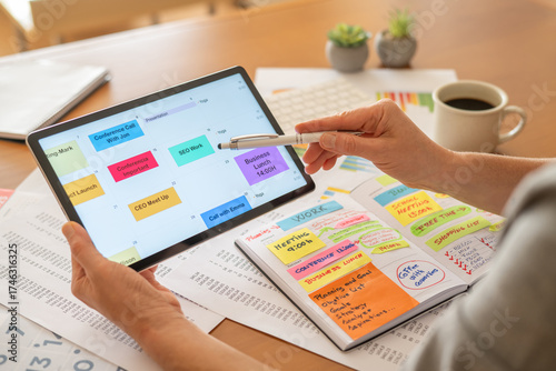 Person is planning daily tasks, business meetings, and personal appointments with a digital calendar application on a tablet and a physical agenda notebook