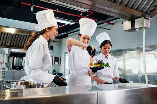Принти на полотні Team of chefs in white uniforms and toques plate gourmet dish in commercial kitchen