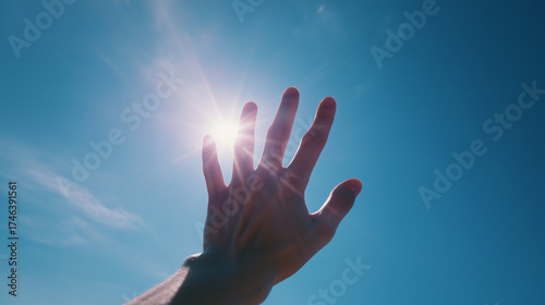 太陽を掴もうとしている手、青空と太陽の光を遮る手のシルエット