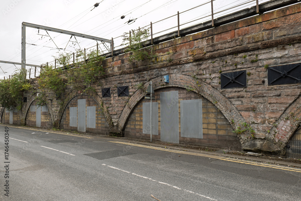 Fototapeta premium Railway viaduct storage arches sealed with doors and metal panels beneath active train tracks, highlighting urban decay, history, and industrial architecture.