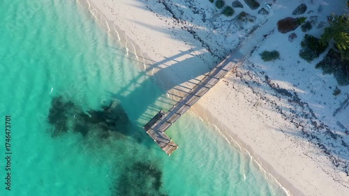 Top-down aerial of a wooden pier with long shadows a sunrise.