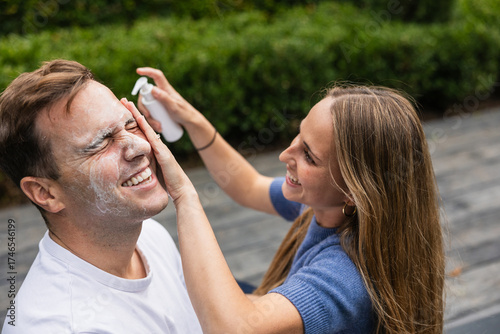 Woman applying sunscreen lotion on man's face outdoors