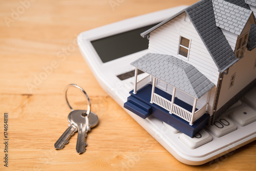 House model on white calculator and house key on wooden table background. Homebuyers, mortgage loan, banking, real estate investment trust (REIT), reverse mortgage, home selling or rental concept.