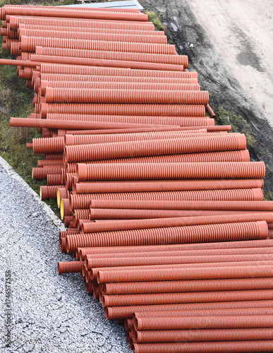 Stacked industrial orange pipes in outdoor construction site setting