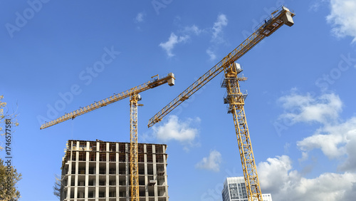 Urban construction site with tower cranes and high rise building against blue sky