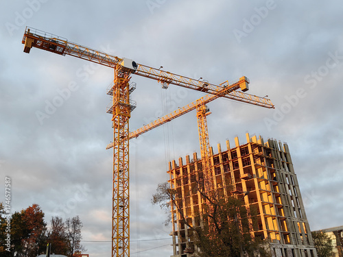 Urban construction scene featuring tower cranes at sunset with partially built structure