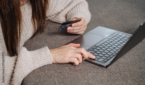 Woman's hand holds a credit or debit bank card while typing on a laptop for a secure online purchase